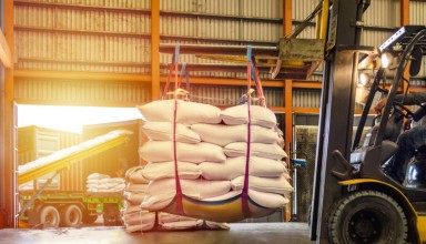 Forklift handling white sugar bags for stuffing into containers outside a warehouse