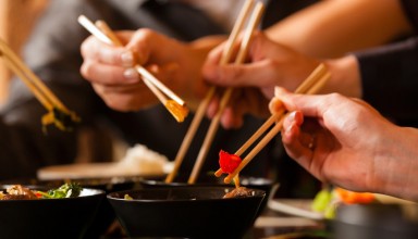 Young people eating in a Thai restaurant, they eating with chopsticks, close-up on hands and food